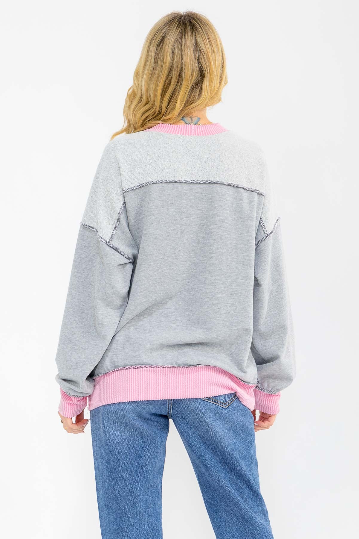woman wearing a gray and pink oversized sweatshirt, viewed from the back, with ribbed cuffs and hem