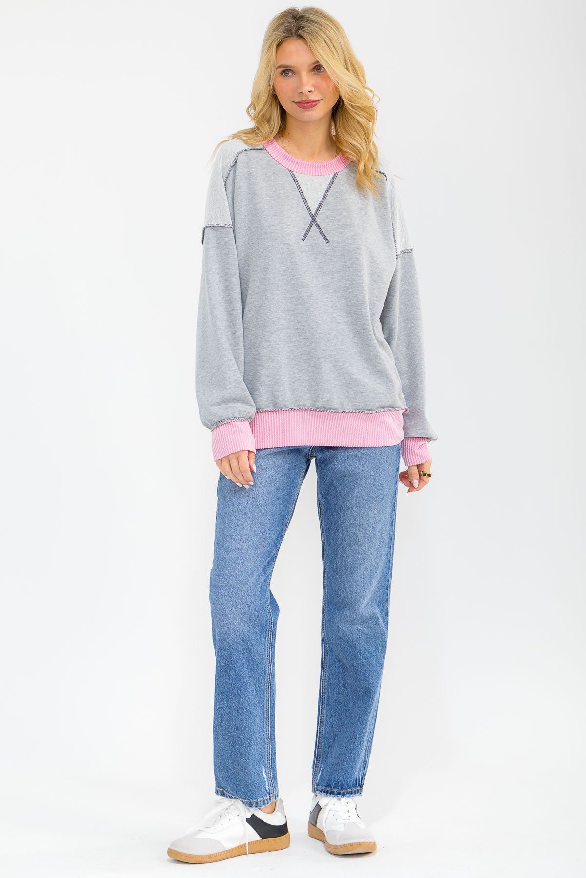 woman wearing a gray sweatshirt with pink accents and ribbed hem paired with blue jeans and white sneakers