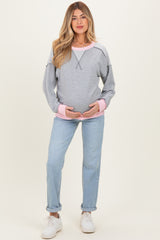 woman wearing a gray maternity sweatshirt with pink details and blue jeans, holding her baby bump