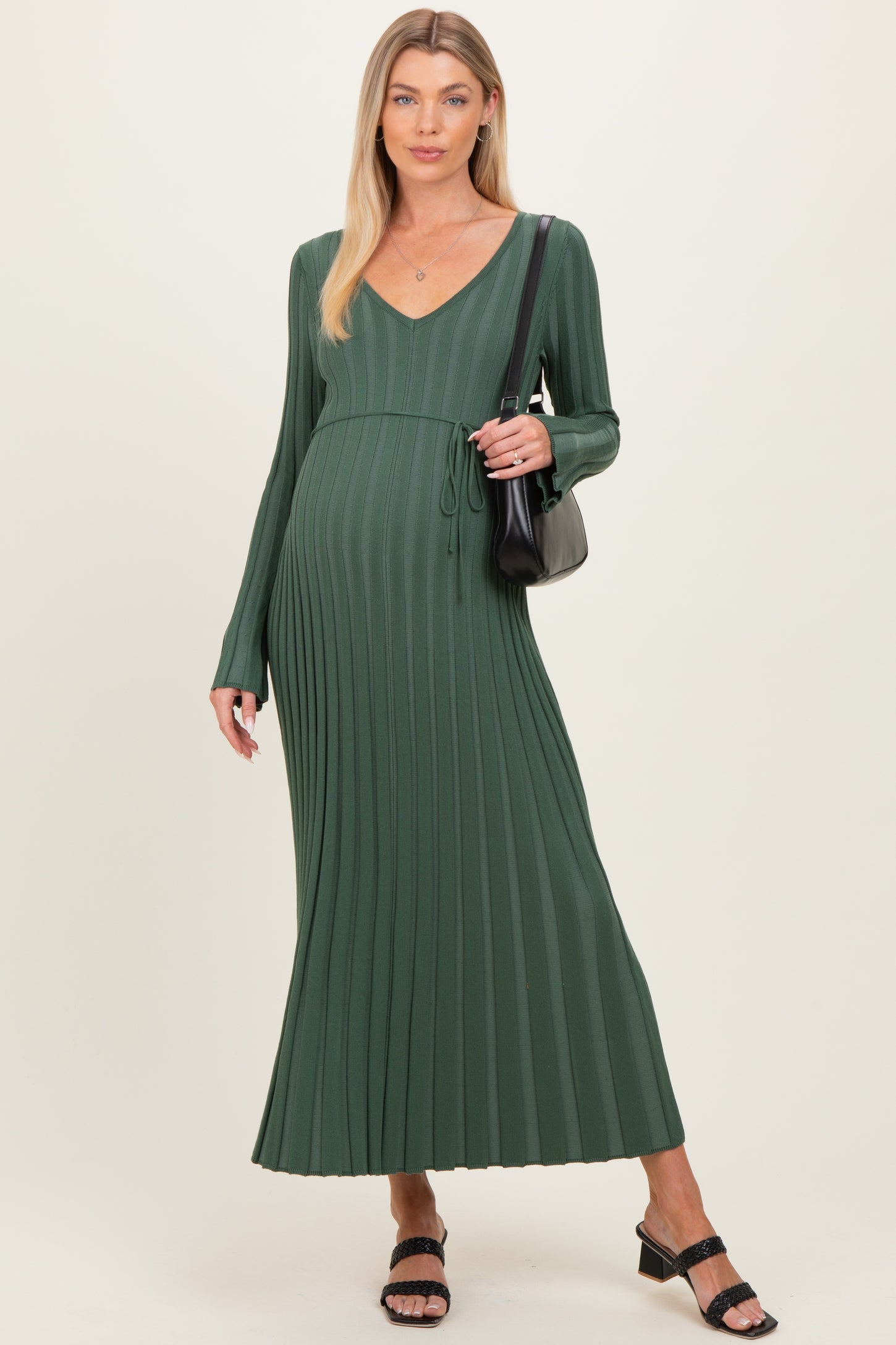 woman wearing a dark green maternity maxi dress with ribbed detailing and a tie waist, carrying a black handbag