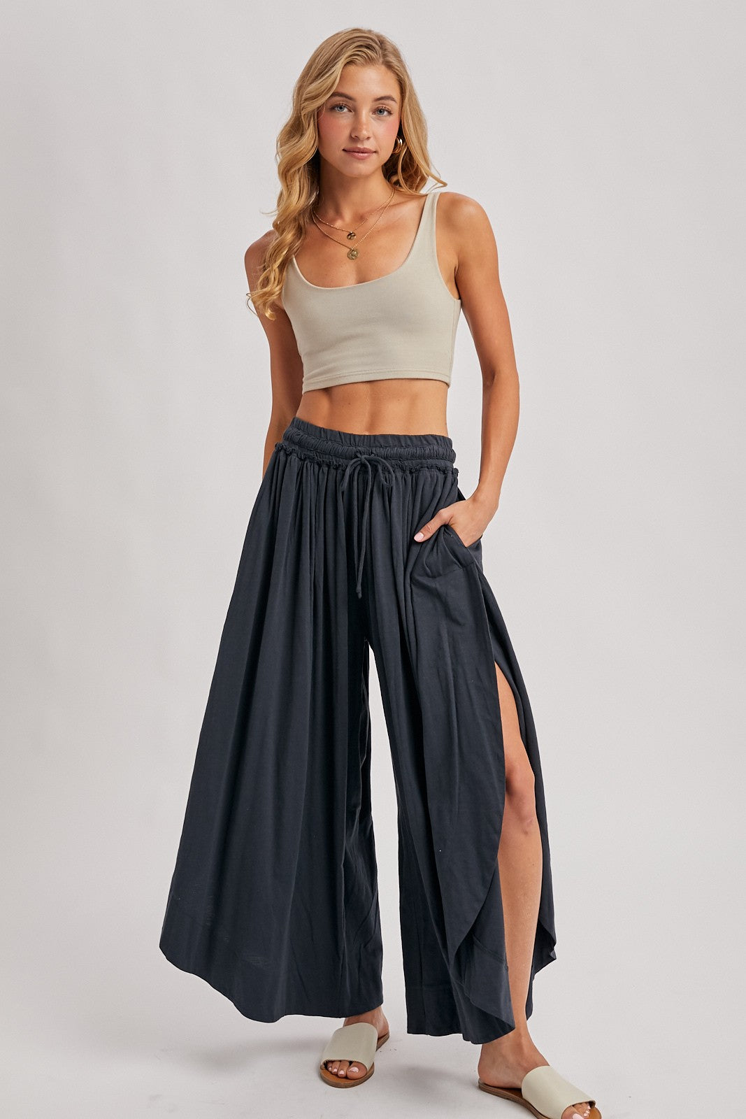 woman wearing a beige crop tank top and dark blue wide-leg pants with side slits