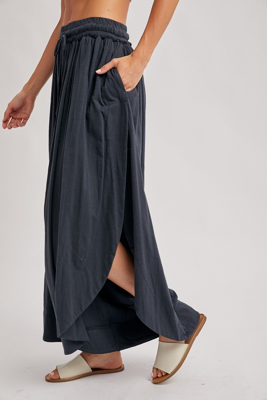 woman wearing a dark gray maxi skirt with side slits and pockets, paired with light-colored slide sandals