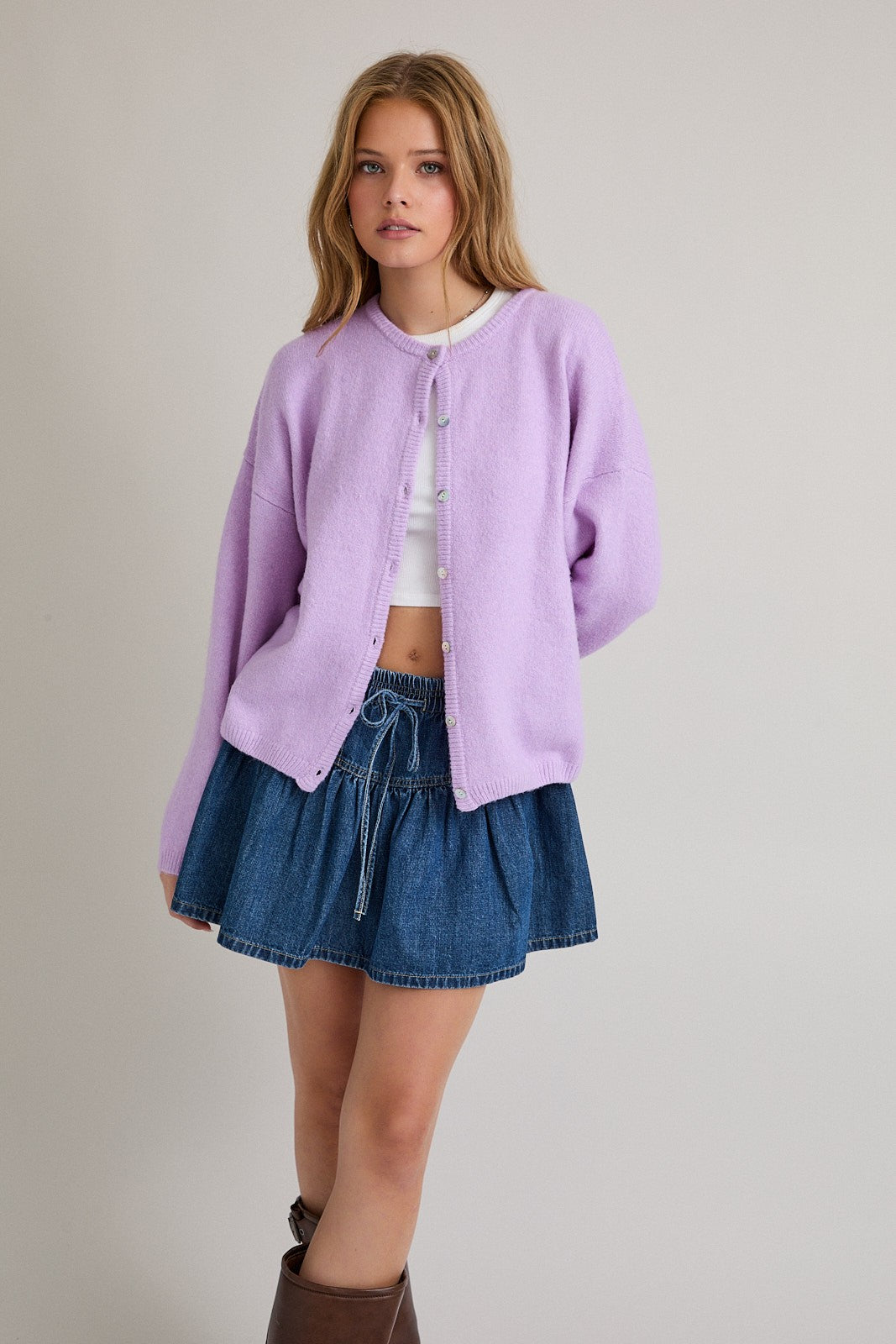 woman wearing a light purple oversized cardigan and a white crop top with a denim mini skirt