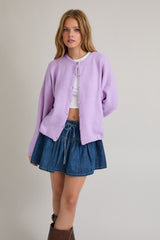 woman wearing a light purple oversized cardigan and a white crop top with a denim mini skirt