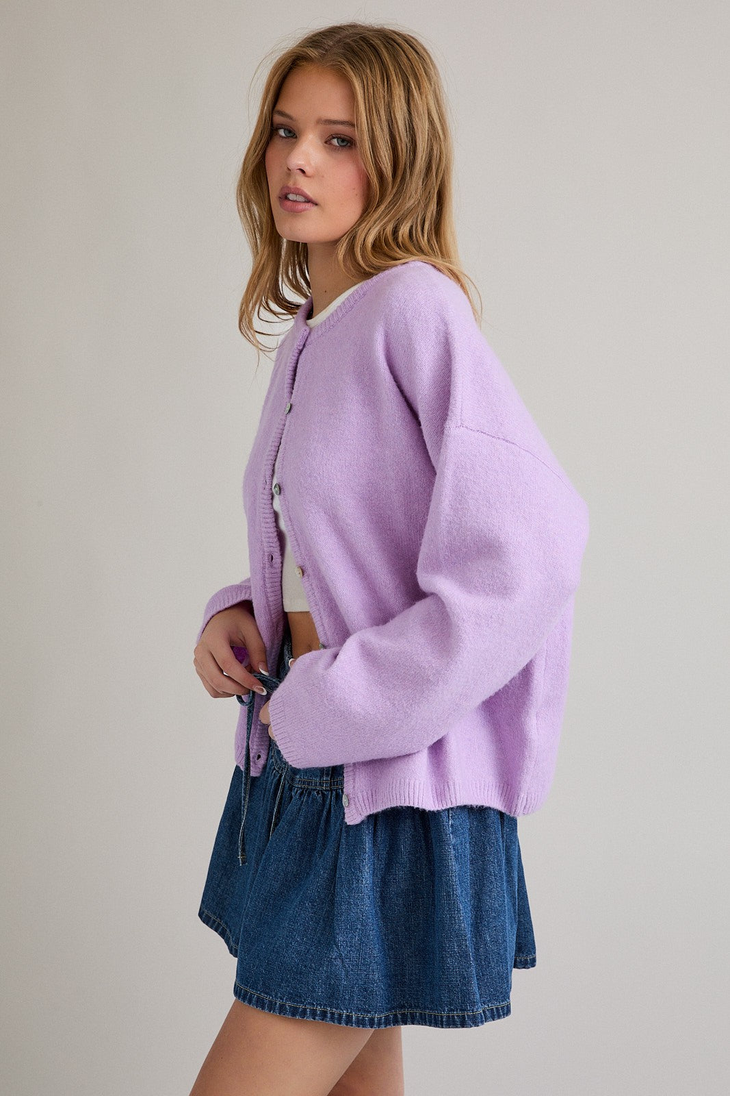 woman wearing a light purple oversized cardigan with buttons and a white crop top, paired with a denim mini skirt