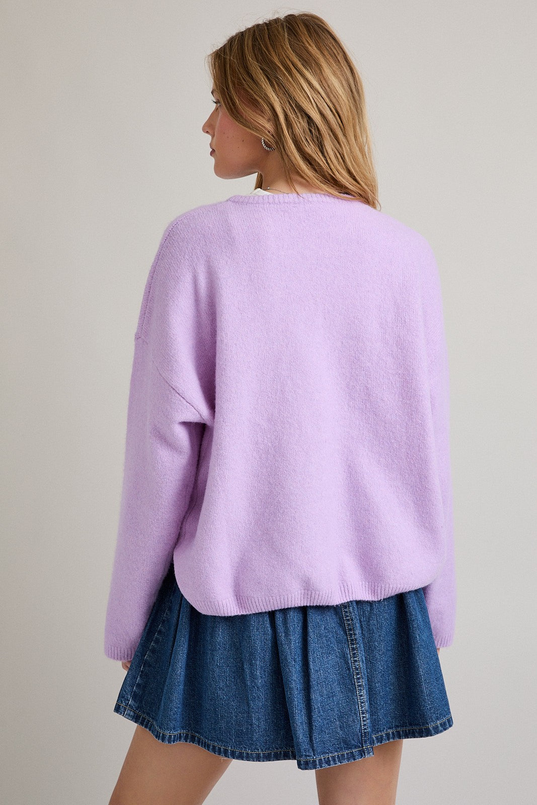 woman wearing a lavender oversized sweater with a round neckline and back view, paired with a denim mini skirt