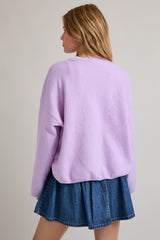 woman wearing a lavender oversized sweater with a round neckline and back view, paired with a denim mini skirt
