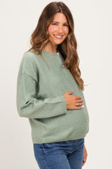 woman wearing a mint green maternity cardigan with buttons, holding her baby bump