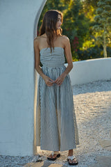 woman wearing a strapless black and white striped maxi dress, standing outdoors against a white wall