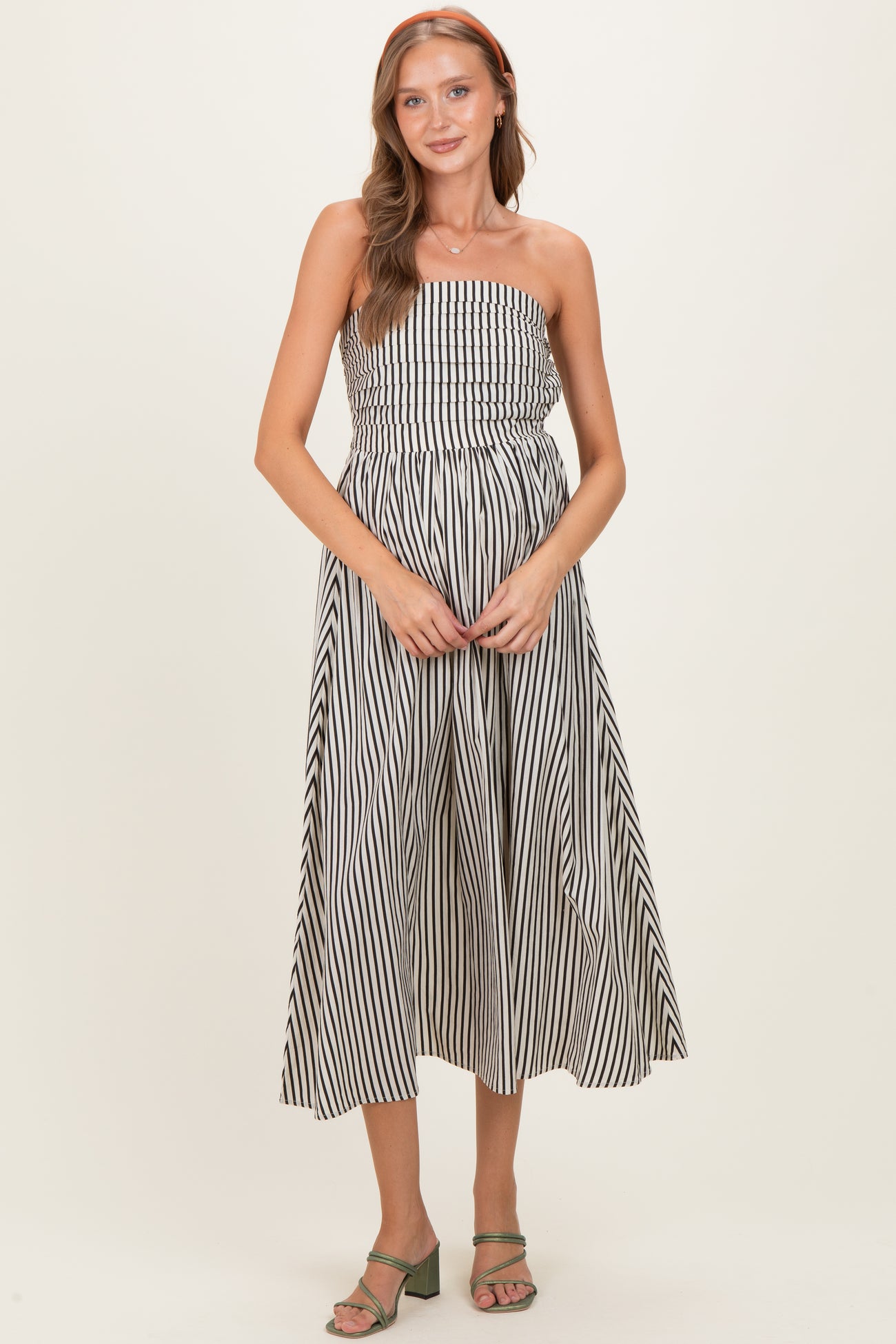 woman wearing a black and white striped strapless maternity maxi dress and holding her baby bump