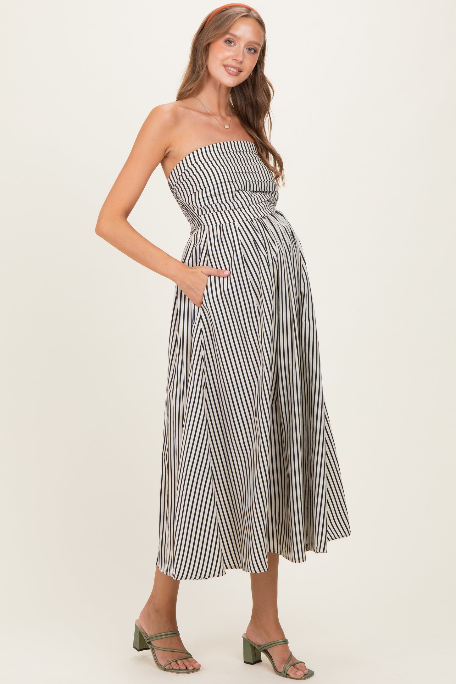 woman wearing a striped strapless maternity dress with pockets and a visible baby bump