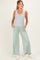 woman wearing a light grey tank top and light green wide-leg maternity pants with pockets and a visible baby bump