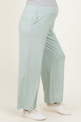 woman wearing light green maternity pants with pockets and a comfortable fit, showing a baby bump