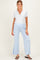 woman wearing a gray henley maternity top and light blue maternity pants with side slits, standing and smiling