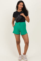 woman wearing green maternity shorts with pockets, styled with a black t-shirt and a small black bag