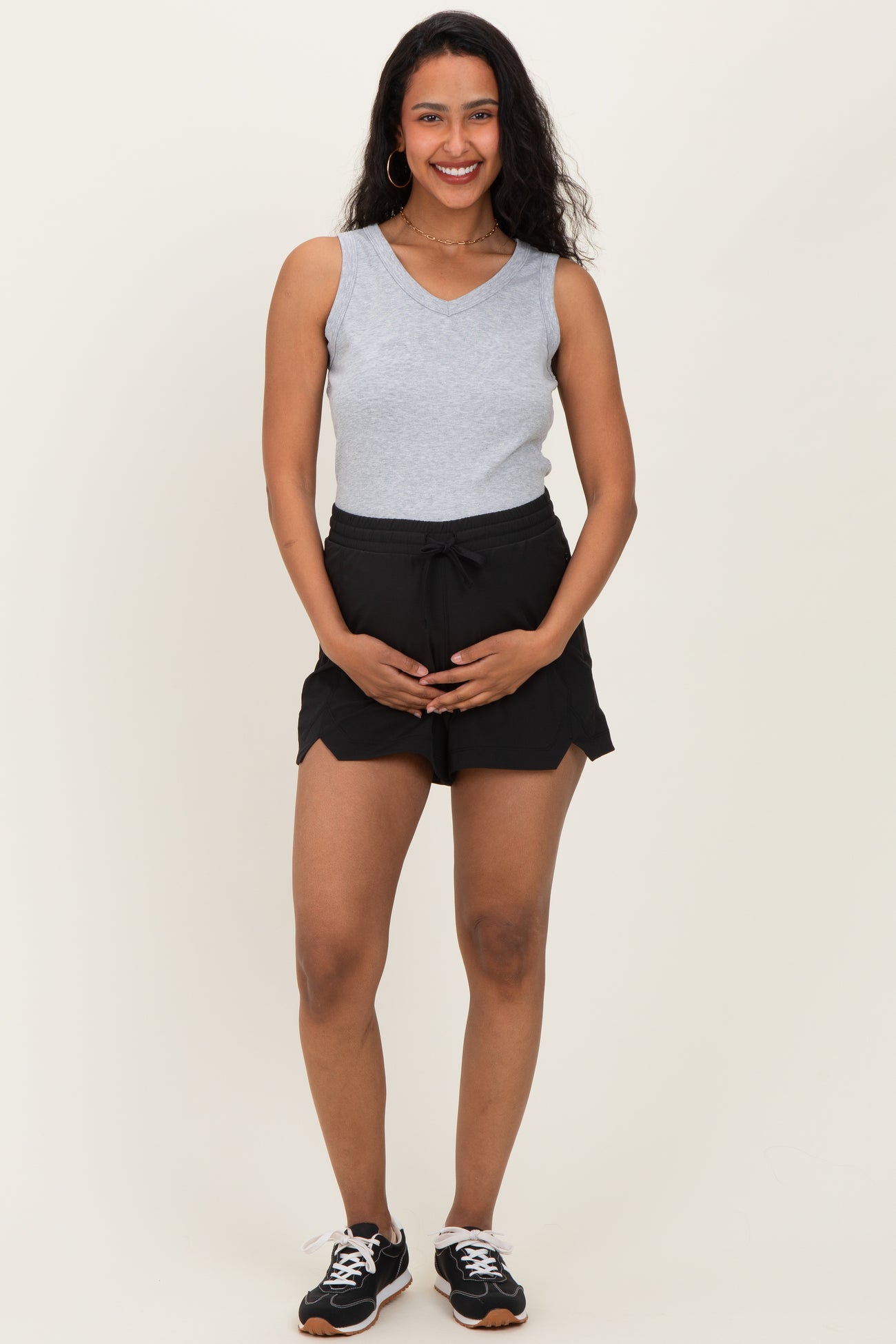 woman wearing a gray sleeveless top and black maternity shorts, holding her baby bump