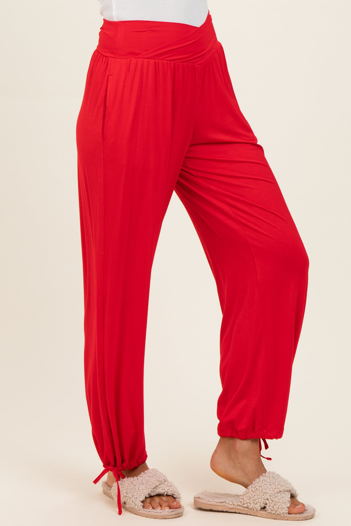 woman wearing red loose-fit jogger pants with elastic waistband and cinched ankles, paired with fuzzy slippers