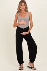 woman wearing a gray maternity bodysuit and black maternity harem pants, holding her baby bump