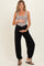 woman wearing a gray maternity bodysuit and black maternity harem pants, holding her baby bump