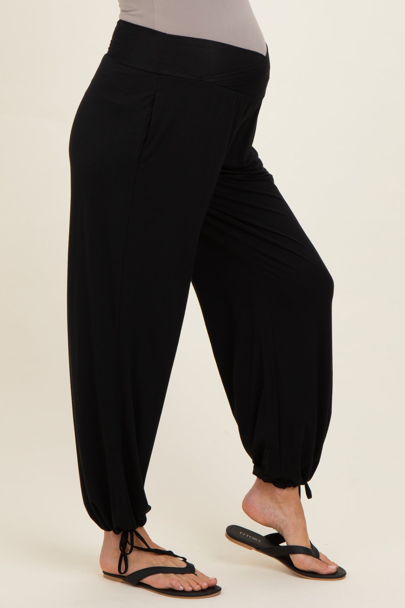 woman wearing black maternity harem pants with a stretchy waistband and cinched ankles, model is barefoot in flip flops