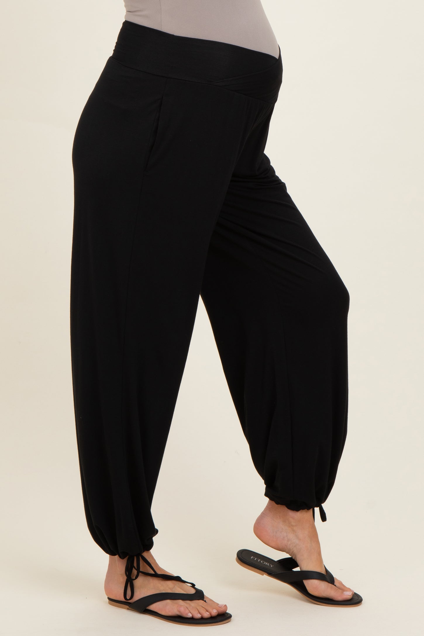 woman wearing black maternity harem pants with a stretchy waistband and cinched ankles, model is barefoot in flip flops