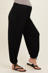 woman wearing black maternity harem pants with a stretchy waistband and cinched ankles, model is barefoot in flip flops