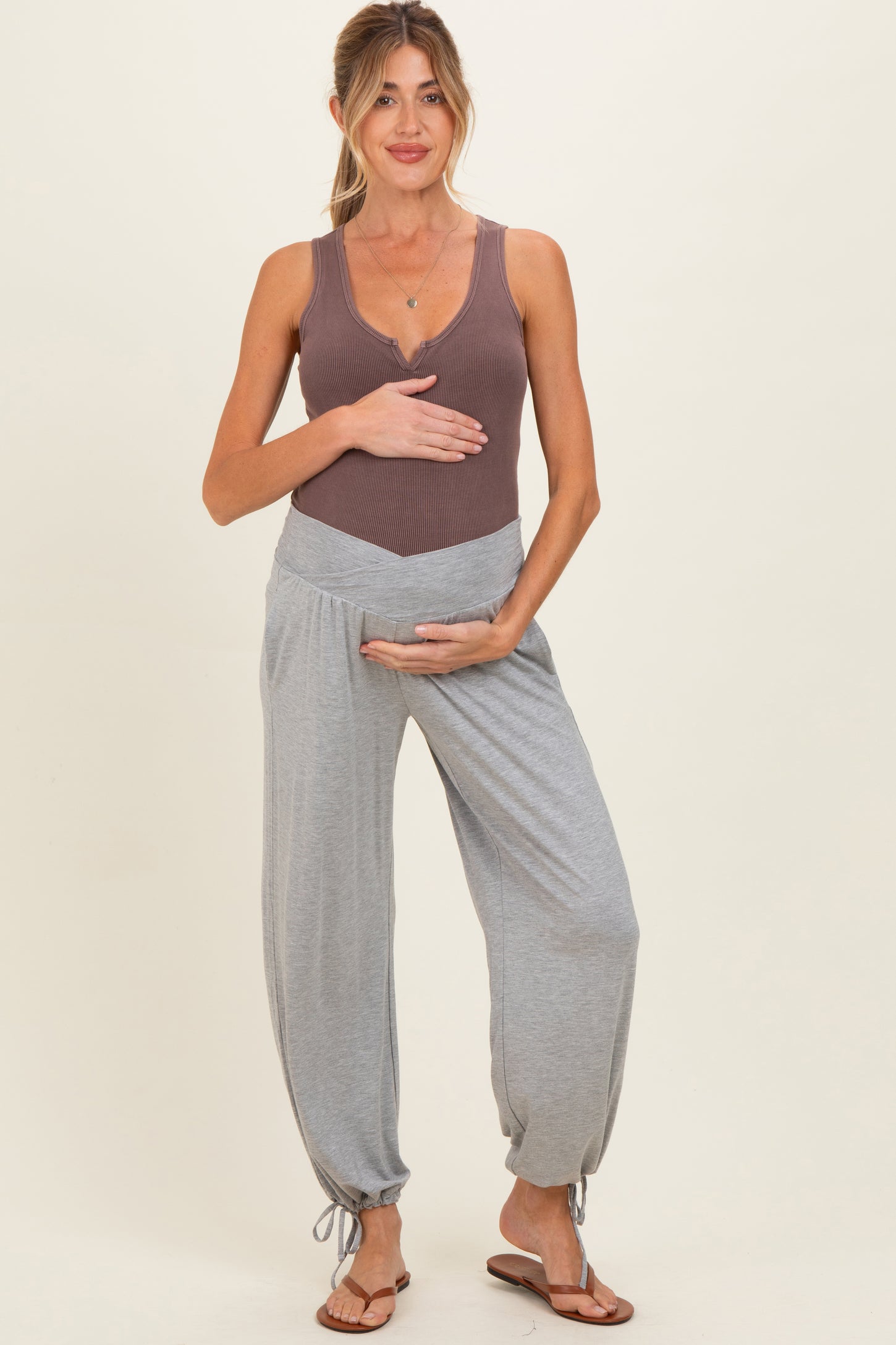 woman wearing a brown ribbed maternity tank top and gray maternity joggers, holding her baby bump