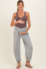 woman wearing a brown ribbed maternity tank top and gray maternity joggers, holding her baby bump