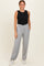 woman wearing a black sleeveless top and light gray wide-leg pants with side pockets, standing against a neutral background