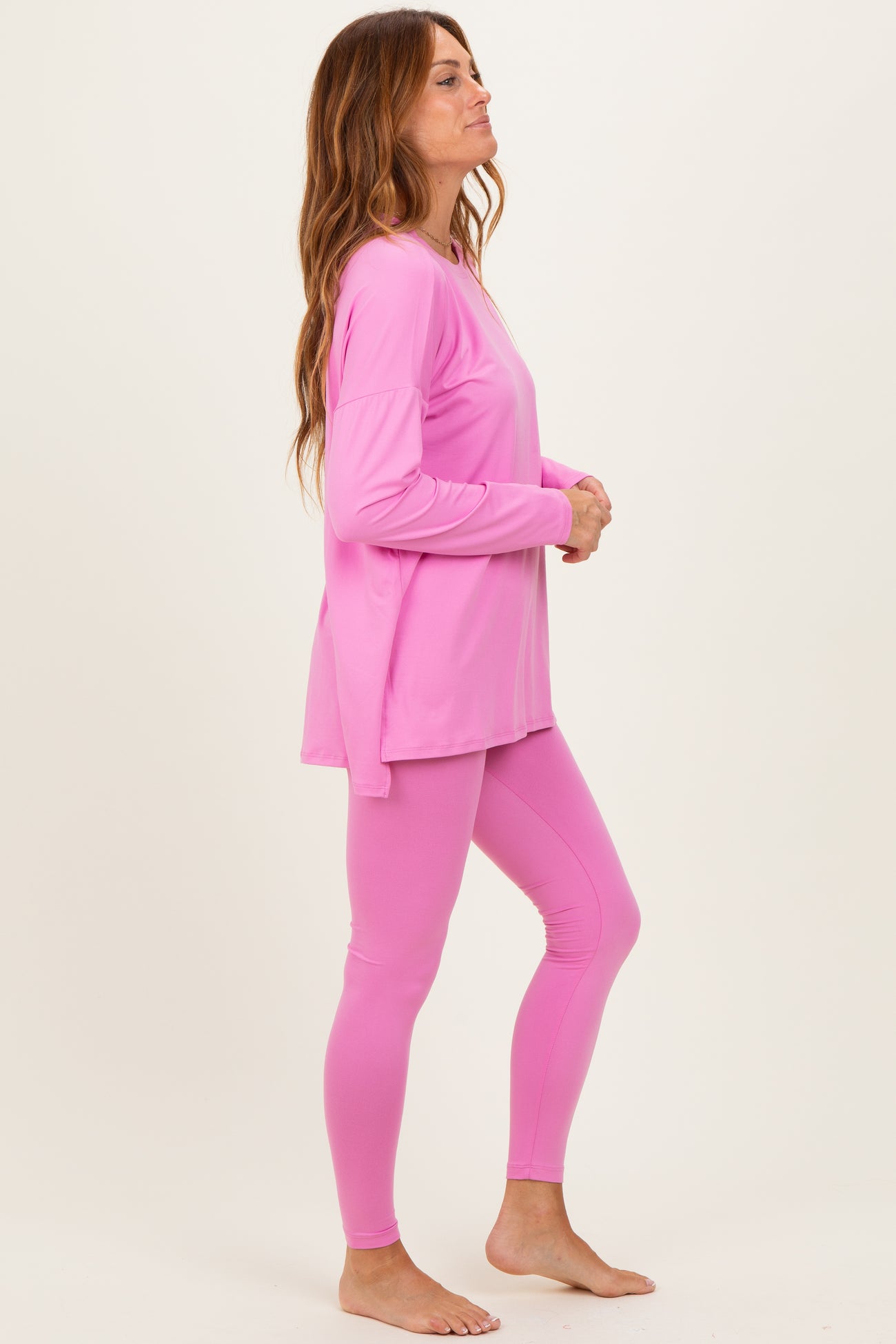 woman wearing a pink long sleeve top and matching leggings, standing sideways with a relaxed pose
