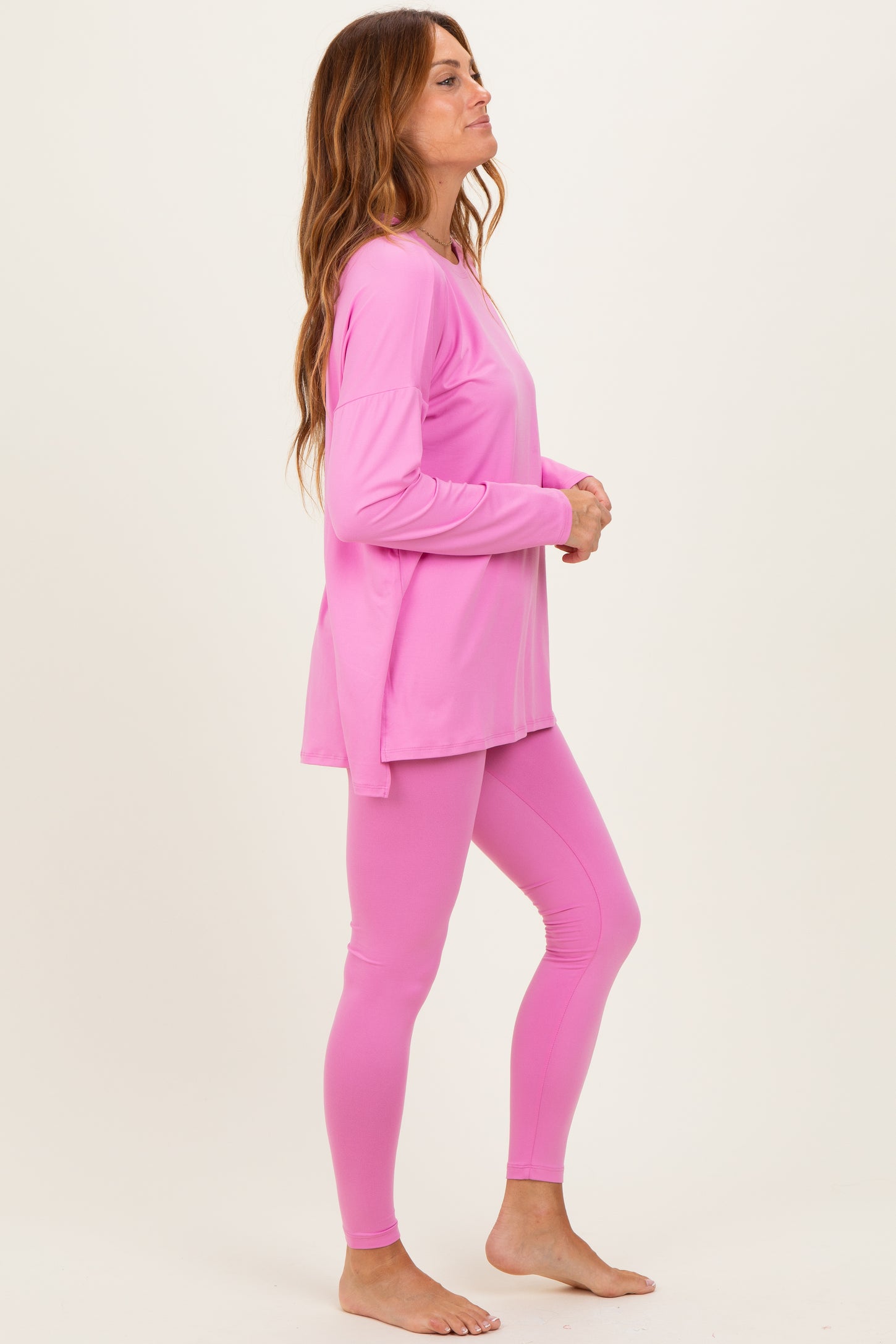 woman wearing a pink long sleeve top and matching leggings, standing sideways with a relaxed pose