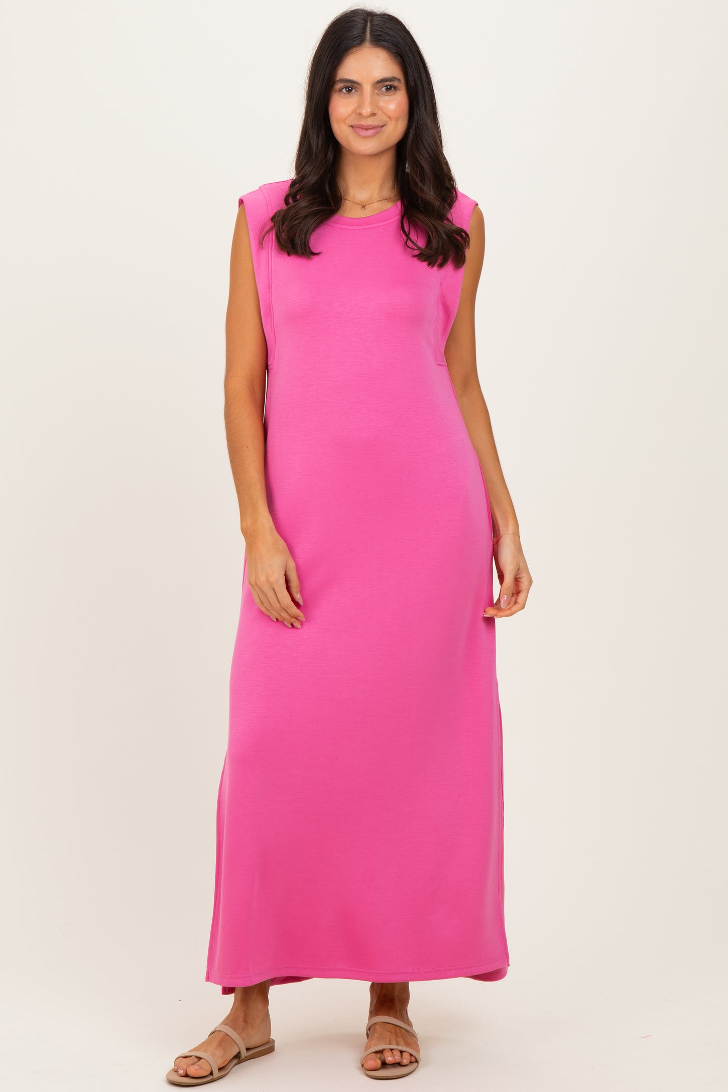 woman wearing a bright pink sleeveless maxi dress standing against a neutral background