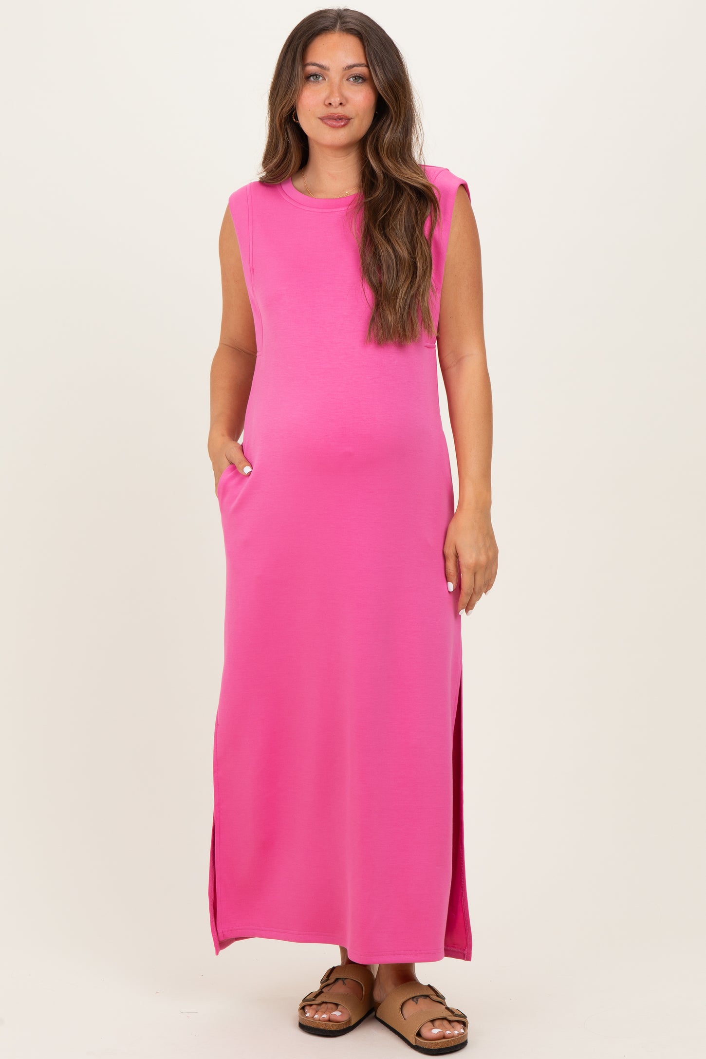 woman wearing a bright pink sleeveless maternity maxi dress with side pockets and a relaxed fit, showing her baby bump