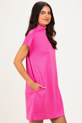 woman wearing a bright pink short sleeve dress with a mock neck and side pockets