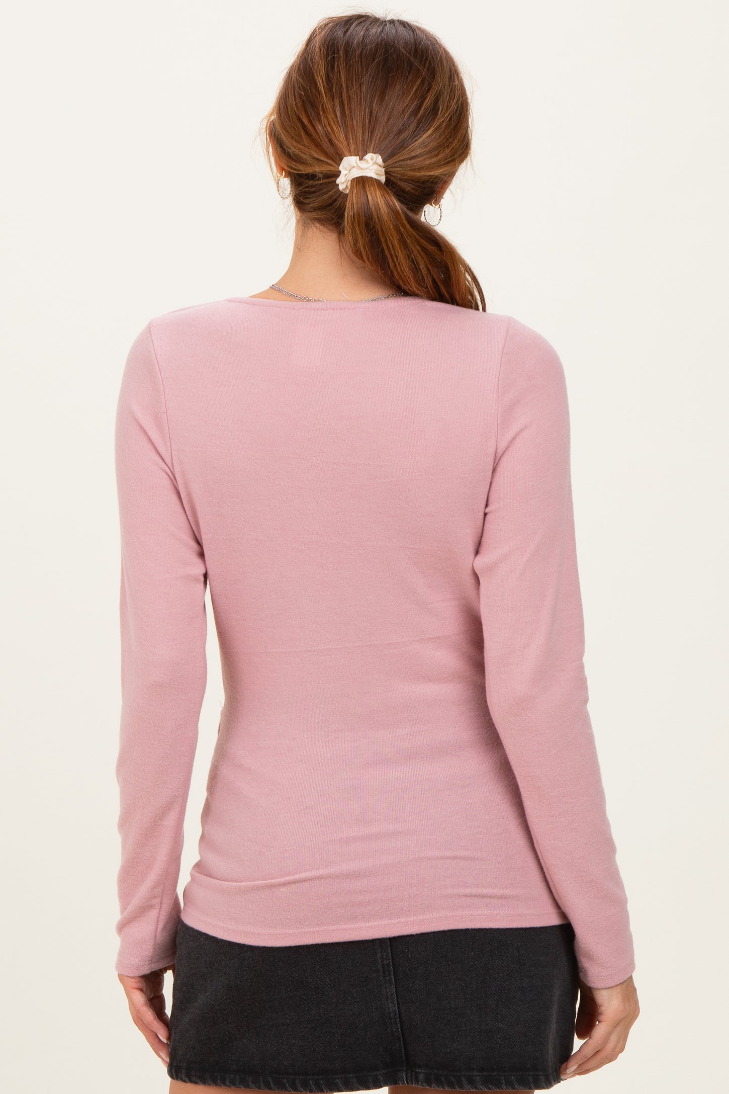 woman wearing a light pink long sleeve top with a fitted style, shown from the back