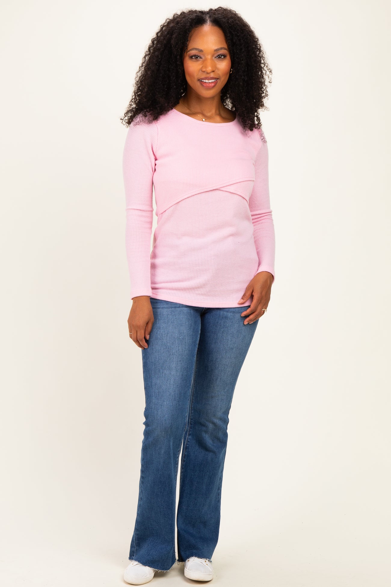woman wearing a light pink long sleeve top with a crossover design and paired with flared blue jeans