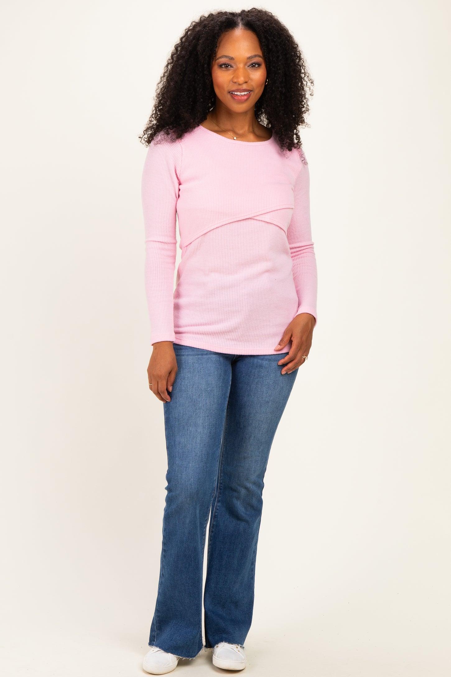 woman wearing a light pink long sleeve top with a crossover design and paired with flared blue jeans