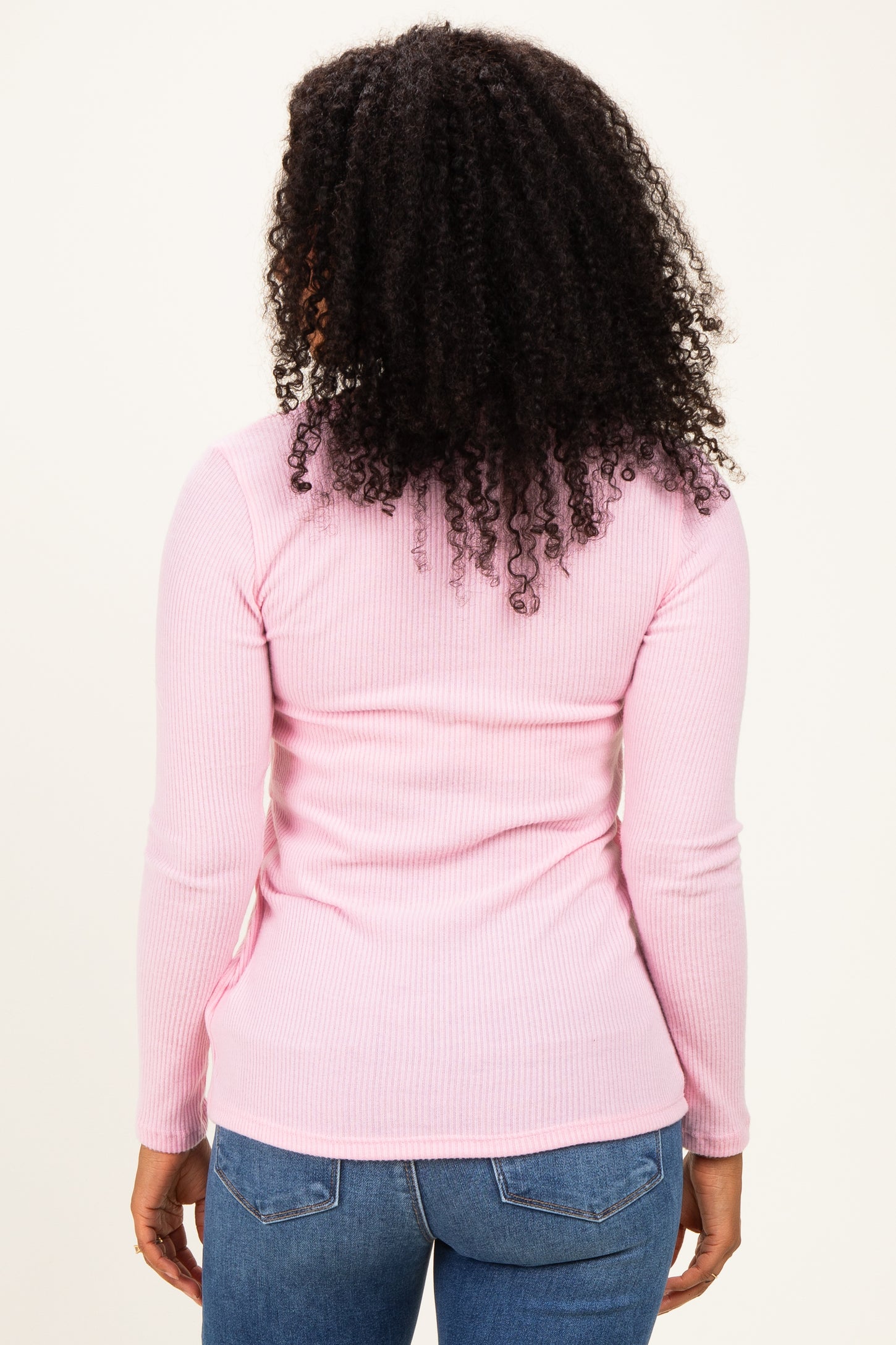 woman wearing a fitted light pink ribbed long sleeve top with a round neckline and back detail, styled with blue jeans