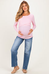 woman wearing a light pink long sleeve maternity top and blue jeans, holding her baby bump