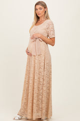 woman wearing a beige lace maternity gown with short sleeves, gently holding her baby bump