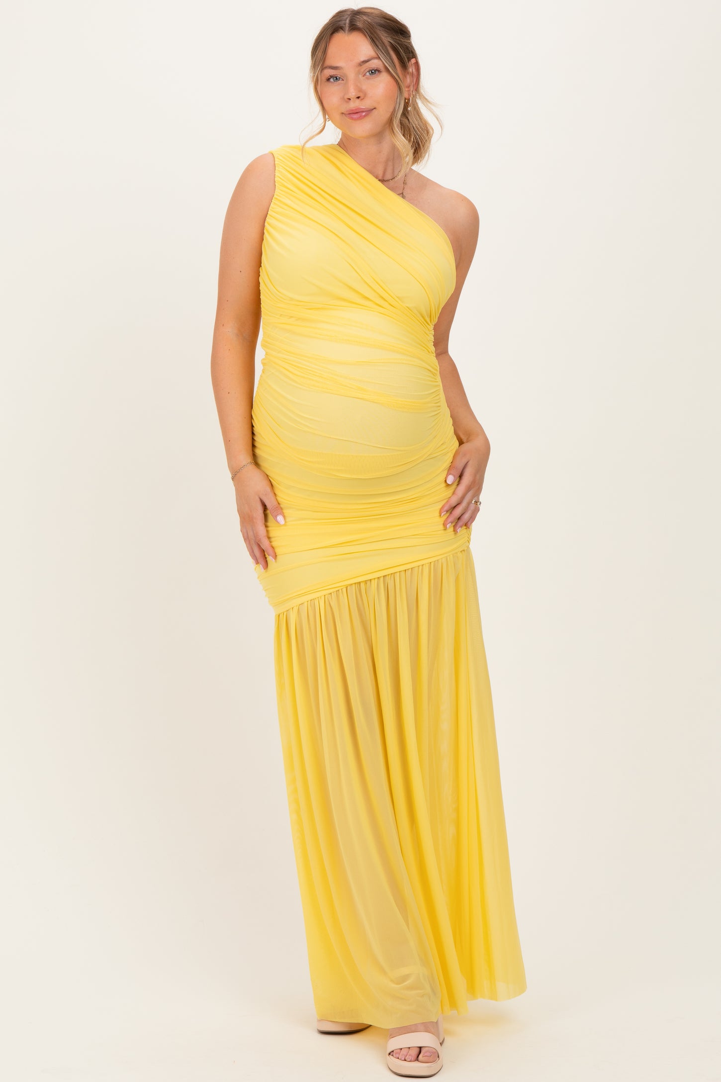 woman wearing a yellow one-shoulder maternity dress with ruched detailing and a flowing skirt, showcasing her baby bump