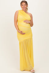 woman wearing a yellow one-shoulder maternity dress with a ruched bodice and flowing skirt, holding her baby bump