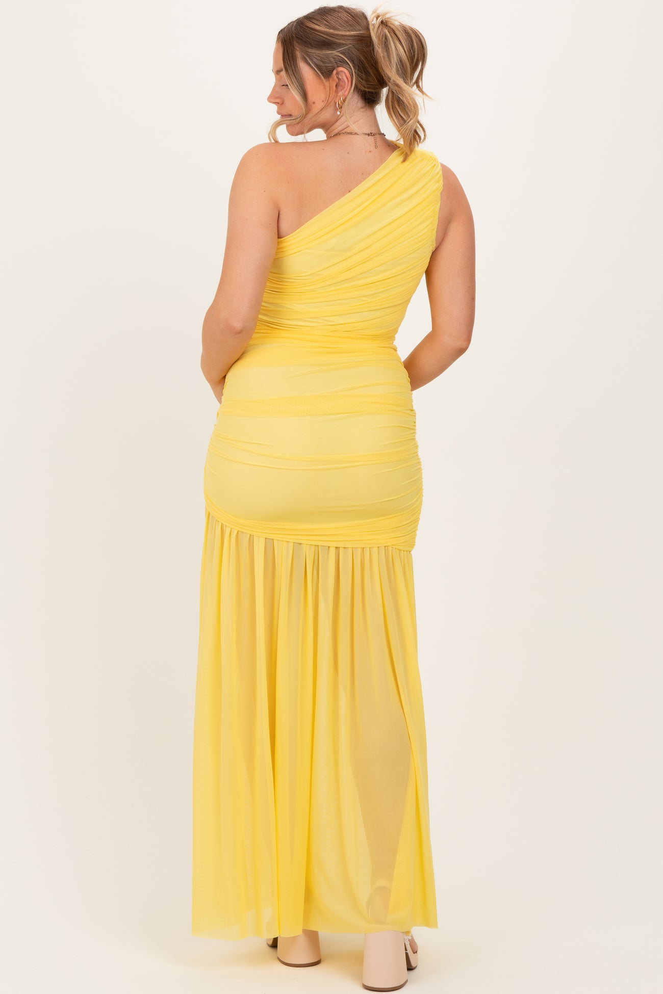 woman wearing a yellow one-shoulder maternity maxi dress with ruching and flowing bottom, showing her baby bump