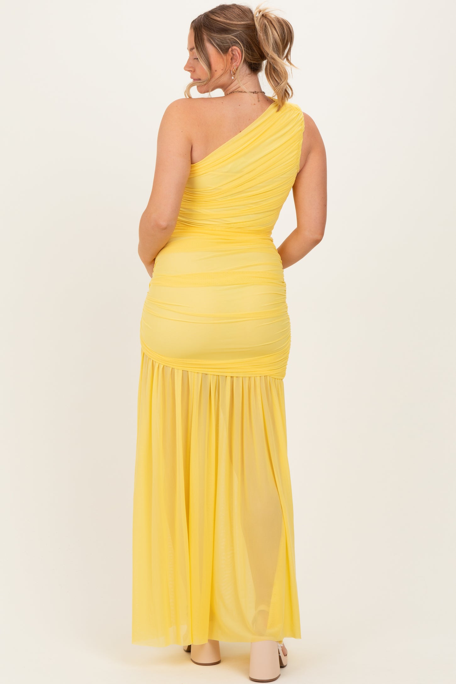 woman wearing a yellow one-shoulder maternity maxi dress with ruching and flowing bottom, showing her baby bump