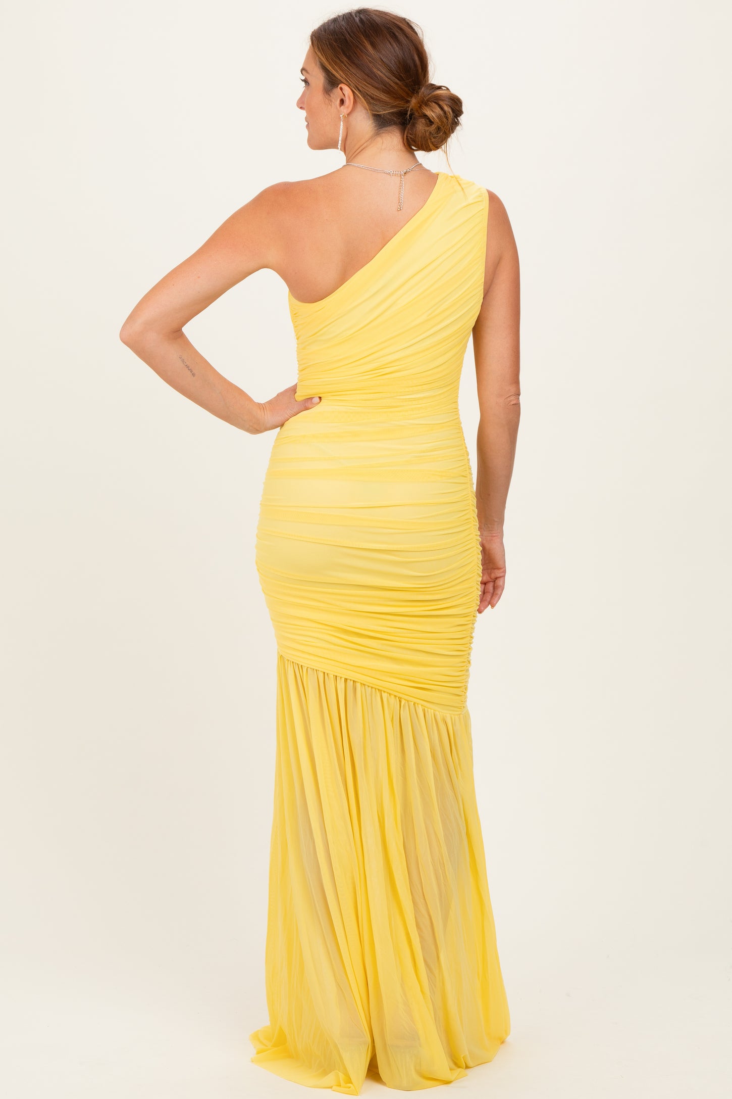 woman wearing a yellow one-shoulder ruched evening gown with a flowing skirt seen from the back