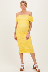 woman wearing a yellow off-shoulder maternity dress with ruched detailing and a visible baby bump