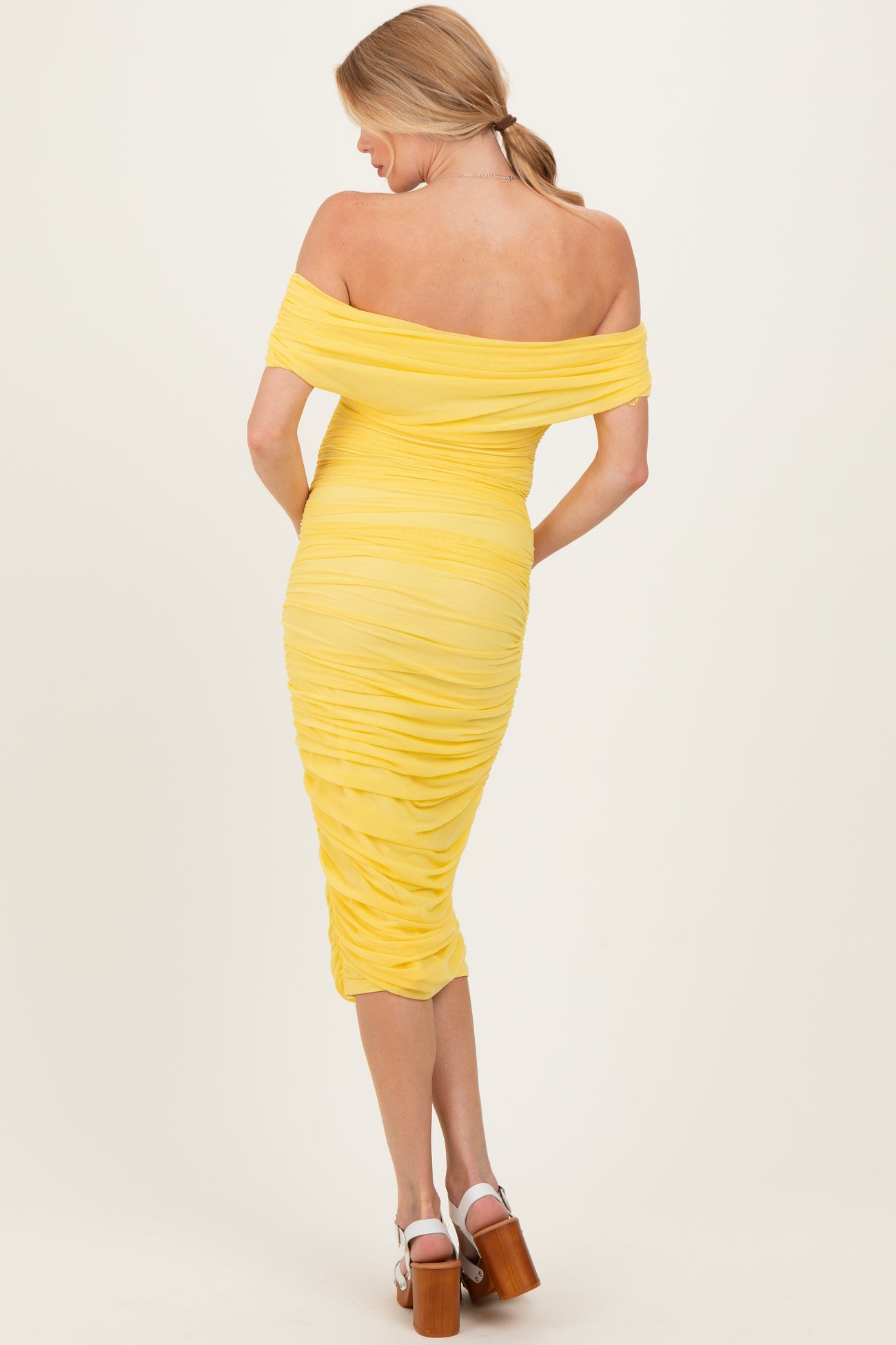 woman wearing a yellow off-shoulder ruched maternity dress, showing a fitted silhouette from the back