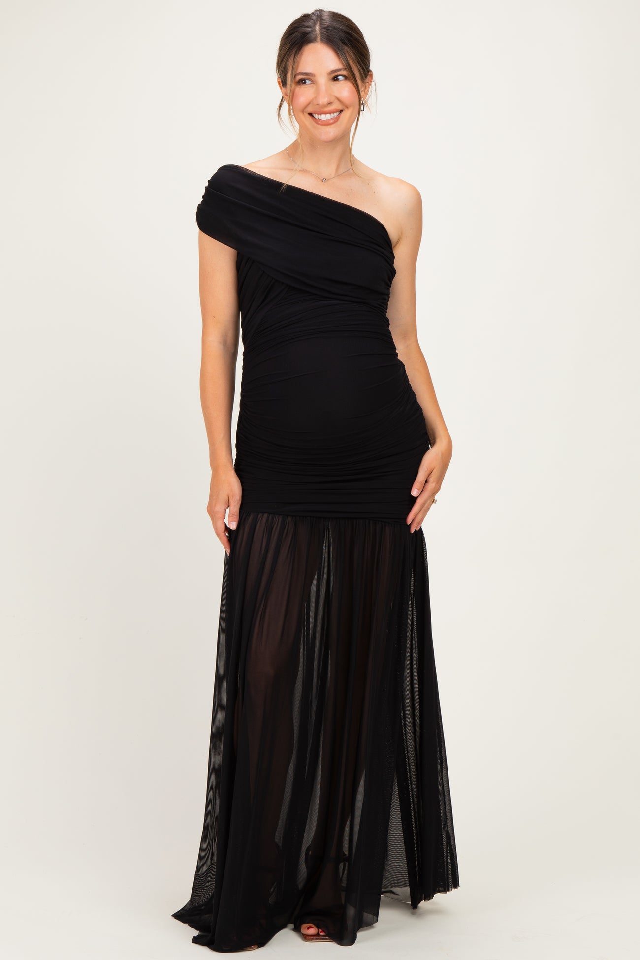 woman wearing a black one-shoulder maternity gown with a fitted bodice and flowy sheer skirt
