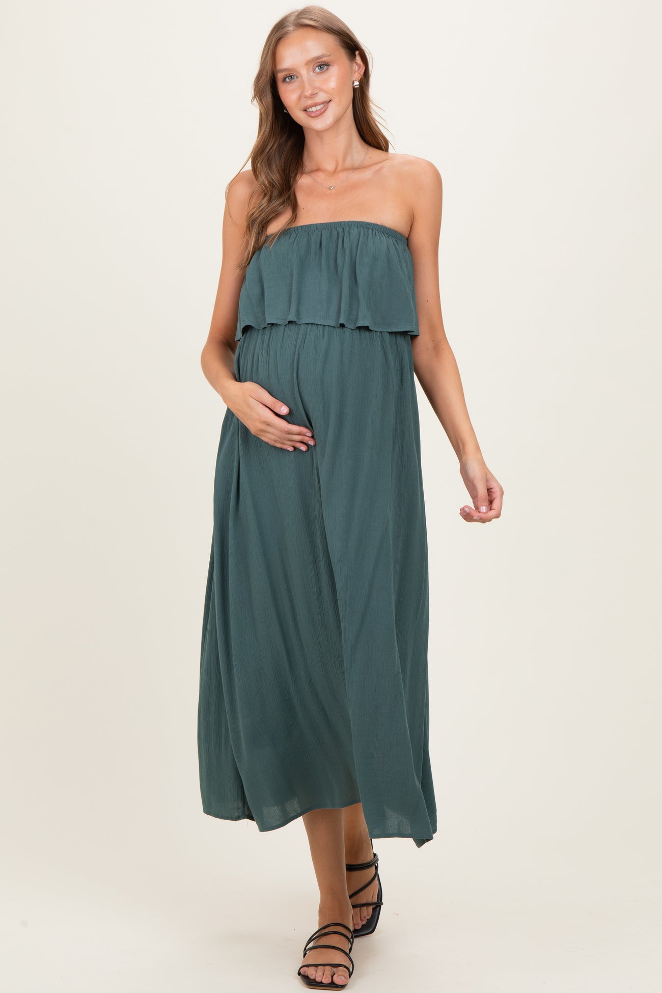 woman wearing a dark teal strapless maternity maxi dress with a ruffled top and holding her baby bump