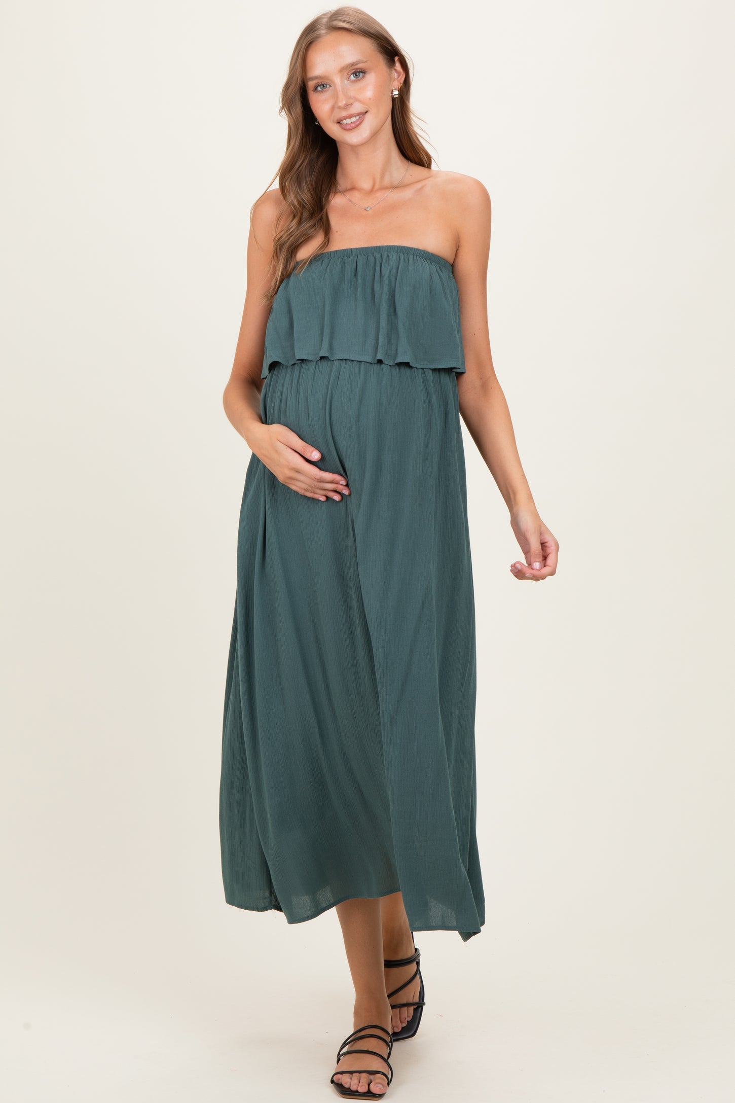 woman wearing a dark teal strapless maternity maxi dress with a ruffled top and holding her baby bump